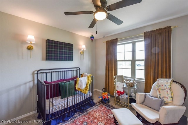 carpeted bedroom with ceiling fan, baseboards, and a nursery area
