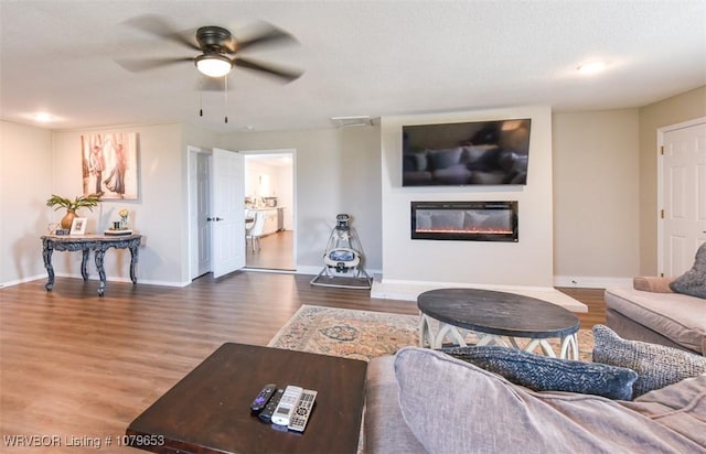 living room with a glass covered fireplace, baseboards, a ceiling fan, and wood finished floors