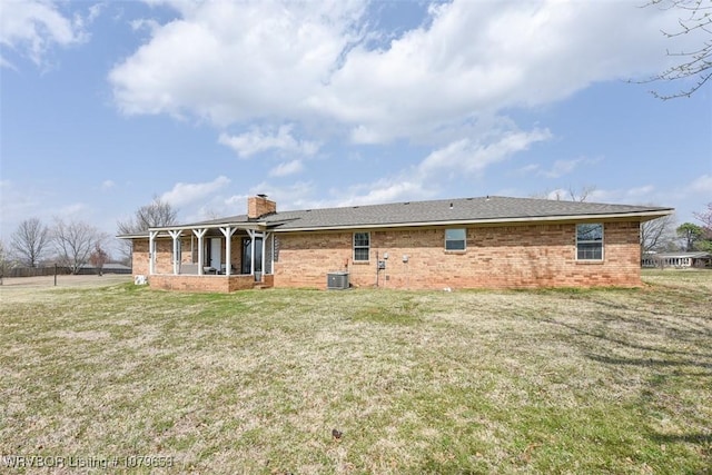 back of property featuring a lawn, brick siding, central AC, and a chimney