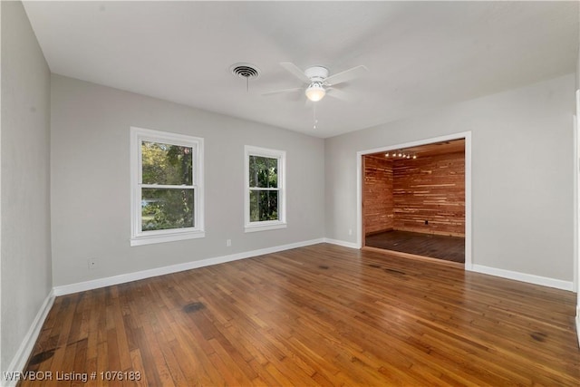 empty room with hardwood / wood-style floors, ceiling fan, and wooden walls