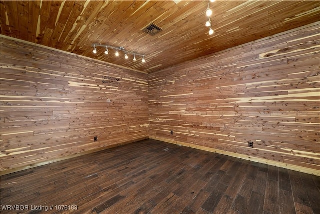 empty room featuring wood walls, dark wood-type flooring, wood ceiling, and track lighting