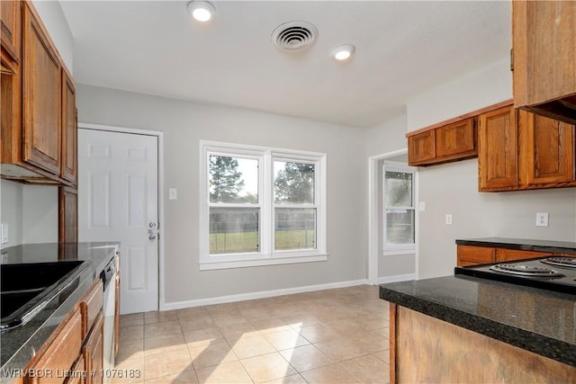 kitchen featuring dark stone counters, sink, light tile patterned floors, and stainless steel dishwasher