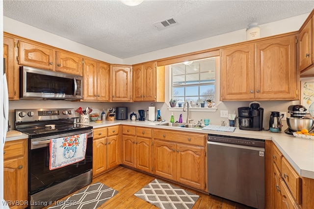 2027 High Meadow Ln, Alma, AR 72921 - kitchen with appliances with stainless steel finishes, light countertops, light wood-style floors, a sink, and a textured ceiling