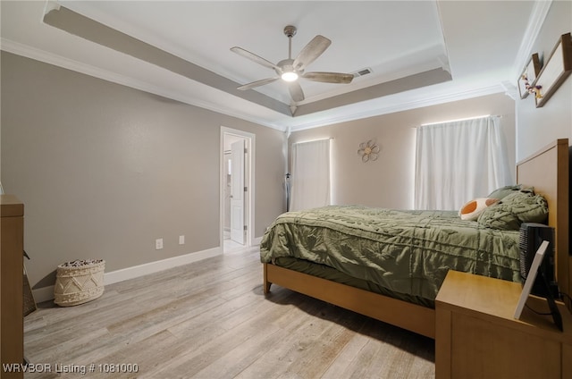 bedroom featuring a raised ceiling, crown molding, wood finished floors, baseboards, and ensuite bath