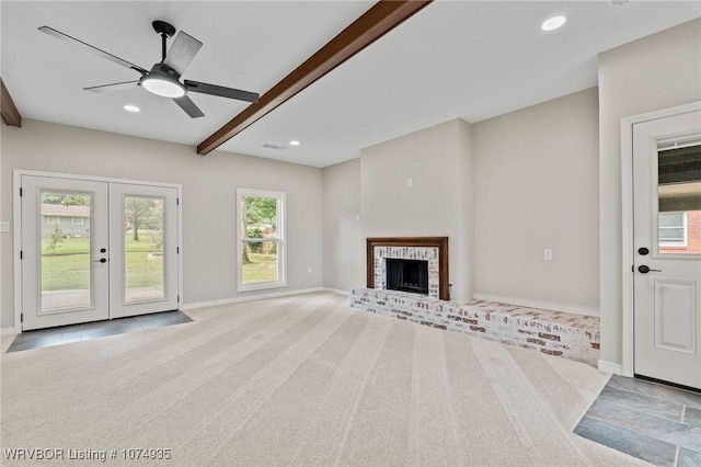 unfurnished living room with beam ceiling, ceiling fan, french doors, a brick fireplace, and light colored carpet