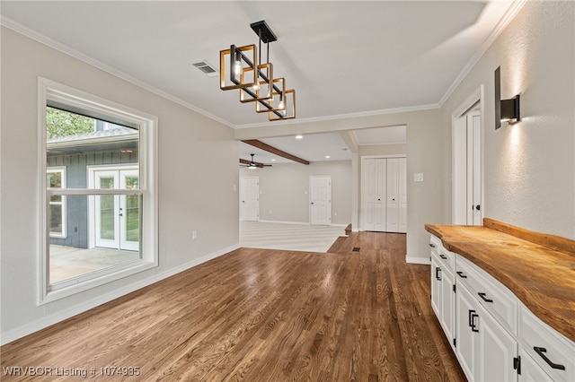 unfurnished dining area featuring beam ceiling, crown molding, dark wood-type flooring, and ceiling fan with notable chandelier