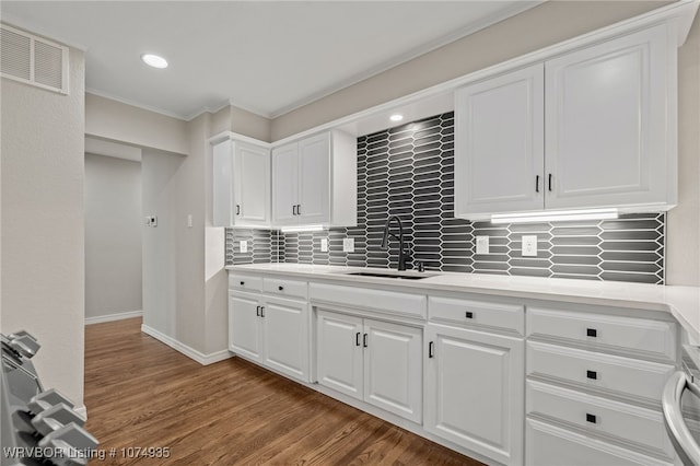 kitchen featuring hardwood / wood-style floors, backsplash, white cabinets, crown molding, and sink