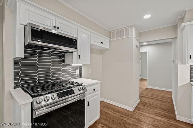 kitchen featuring backsplash, white cabinets, crown molding, hardwood / wood-style flooring, and stainless steel appliances