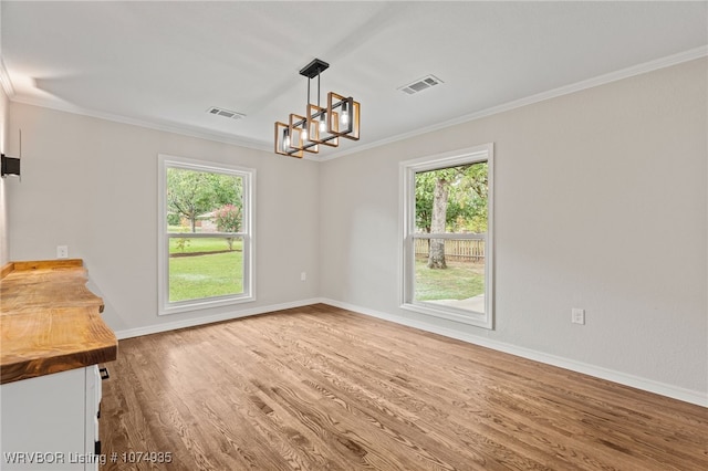 unfurnished dining area with a wealth of natural light, an inviting chandelier, hardwood / wood-style flooring, and ornamental molding