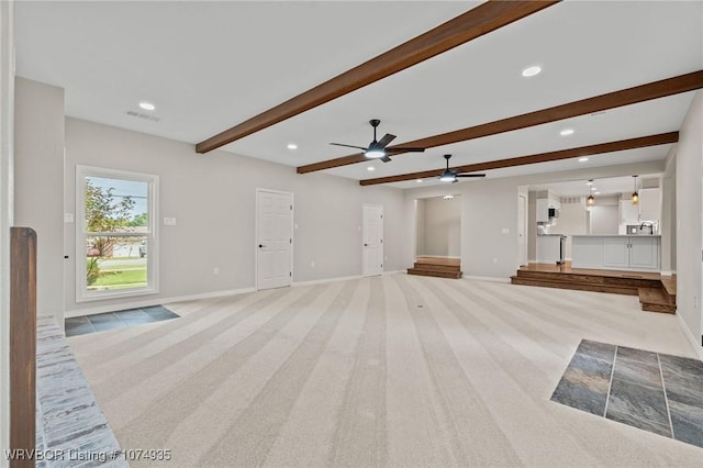 unfurnished living room with ceiling fan, beamed ceiling, and light colored carpet