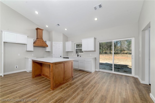 kitchen with a center island, high vaulted ceiling, white cabinets, light hardwood / wood-style flooring, and custom range hood