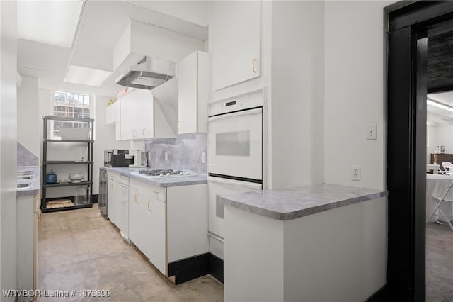 kitchen with wall chimney exhaust hood, stainless steel gas stovetop, white double oven, and white cabinetry