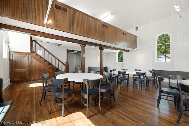 dining space featuring a towering ceiling, dark wood-type flooring, and decorative columns