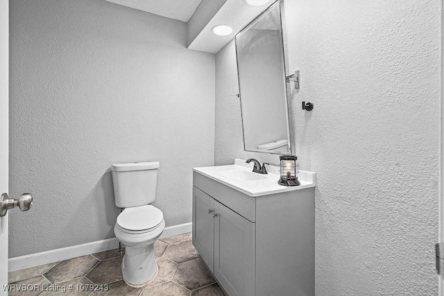 bathroom featuring toilet, a textured wall, baseboards, and vanity