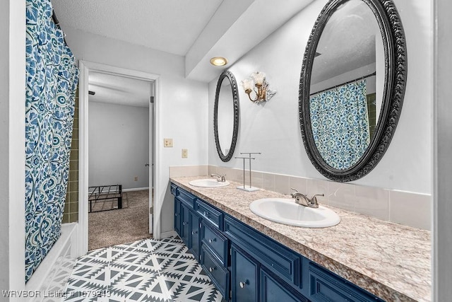 bathroom with a textured ceiling, double vanity, a sink, and baseboards