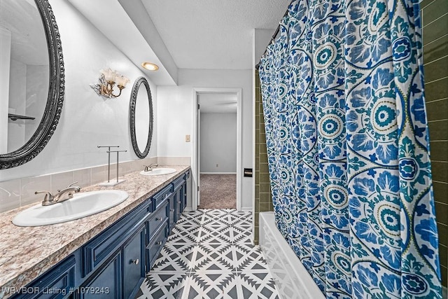 full bathroom with double vanity, shower / bathtub combination with curtain, a textured ceiling, and a sink