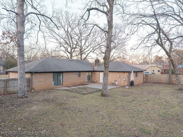 rear view of property featuring a patio, a fenced backyard, a chimney, roof with shingles, and brick siding