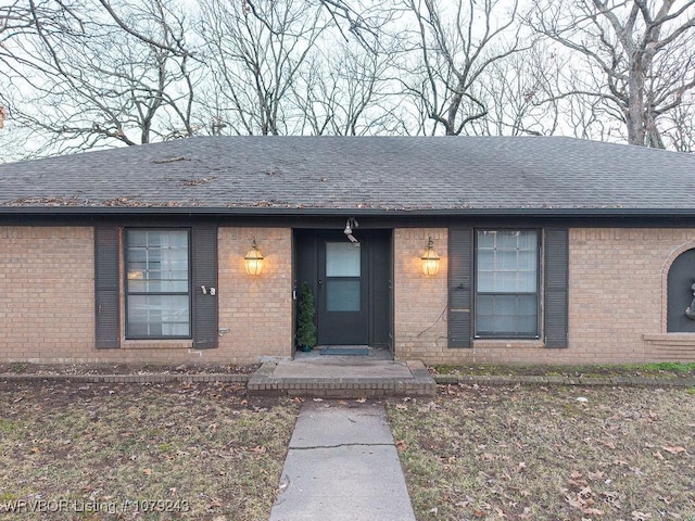 ranch-style house featuring brick siding and roof with shingles