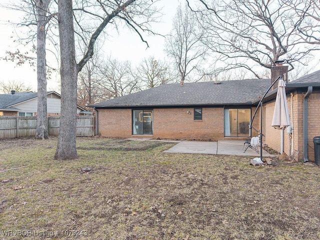 rear view of house featuring a patio, brick siding, fence, roof with shingles, and a lawn