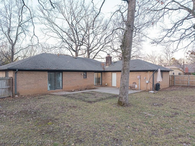 rear view of property featuring a chimney, fence, a yard, a patio area, and brick siding