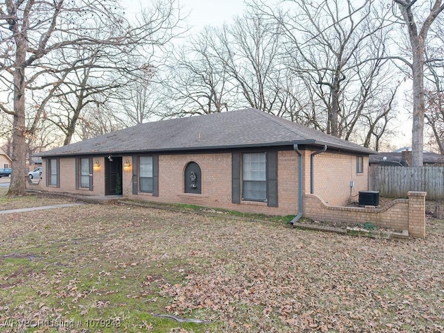 ranch-style home featuring central AC unit, roof with shingles, fence, and brick siding