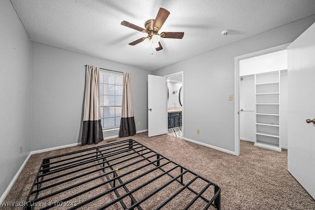 unfurnished bedroom featuring a textured ceiling, carpet floors, a walk in closet, and baseboards