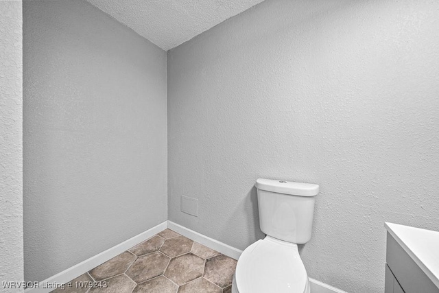 half bath with a textured ceiling, vanity, toilet, and baseboards