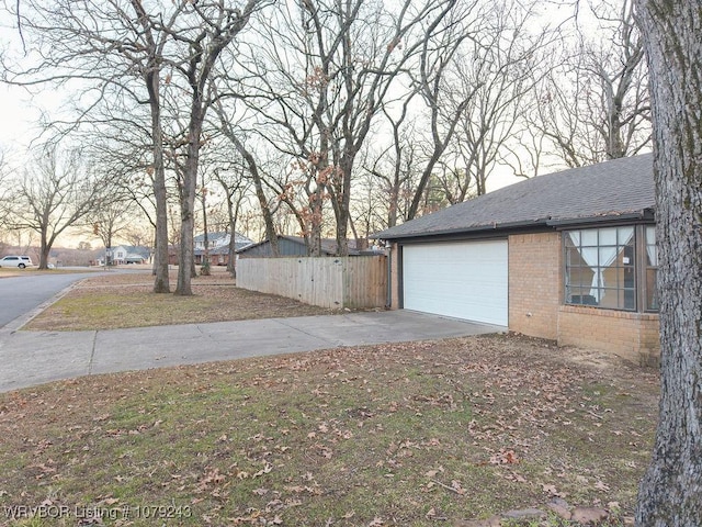 view of property exterior featuring an attached garage, brick siding, fence, concrete driveway, and roof with shingles