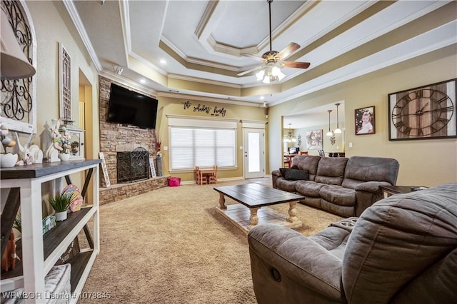 carpeted living room with crown molding, a raised ceiling, a ceiling fan, and a stone fireplace