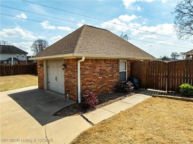 view of side of home with roof with shingles, concrete driveway, fence, brick siding, and a garage
