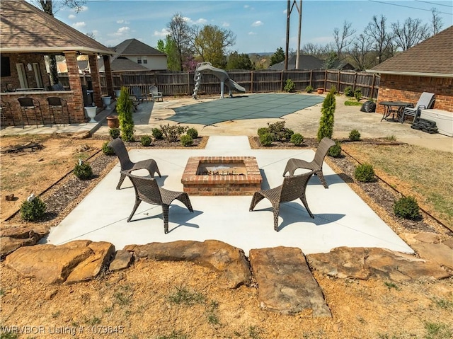 view of swimming pool with a fire pit, a patio area, a water slide, a fenced backyard, and outdoor dry bar