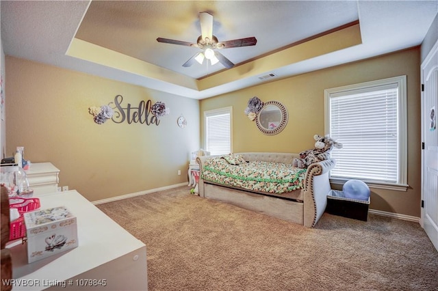 carpeted bedroom with a ceiling fan, a raised ceiling, baseboards, and multiple windows
