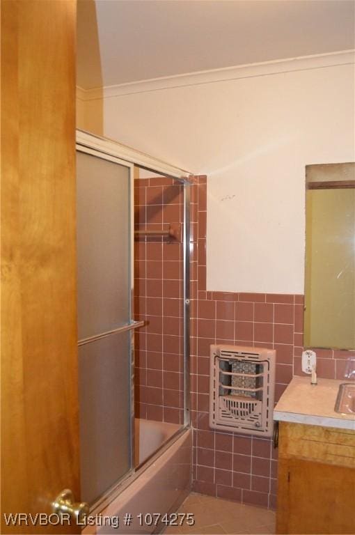 bathroom featuring combined bath / shower with glass door, vanity, heating unit, crown molding, and tile patterned flooring