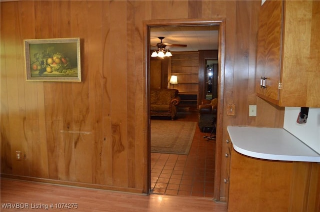 kitchen with light wood-type flooring, ceiling fan, and wood walls