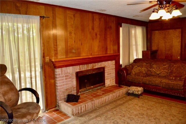 living room with a tiled fireplace, wooden walls, ceiling fan, and a healthy amount of sunlight