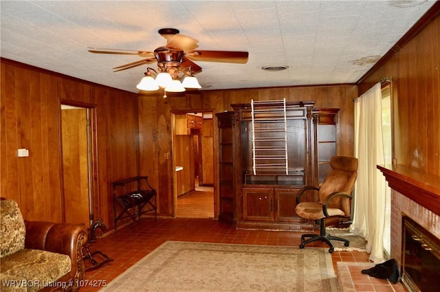 sitting room with ceiling fan, tile patterned flooring, crown molding, a tiled fireplace, and wooden walls