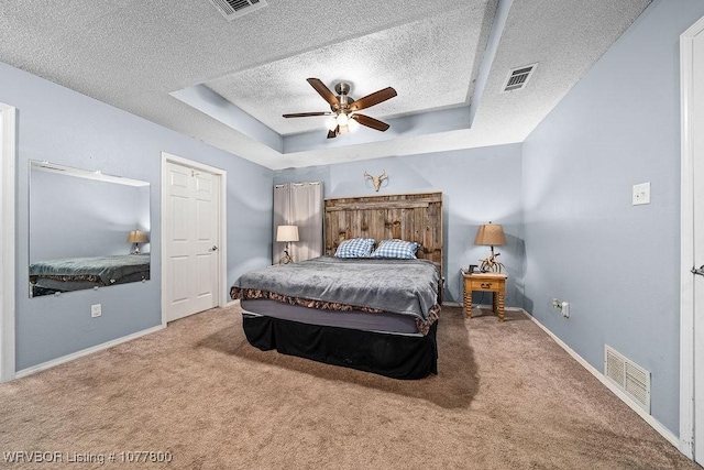 bedroom with a raised ceiling, ceiling fan, carpet flooring, and a textured ceiling