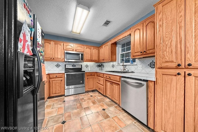 kitchen with stainless steel appliances, tasteful backsplash, sink, and a textured ceiling