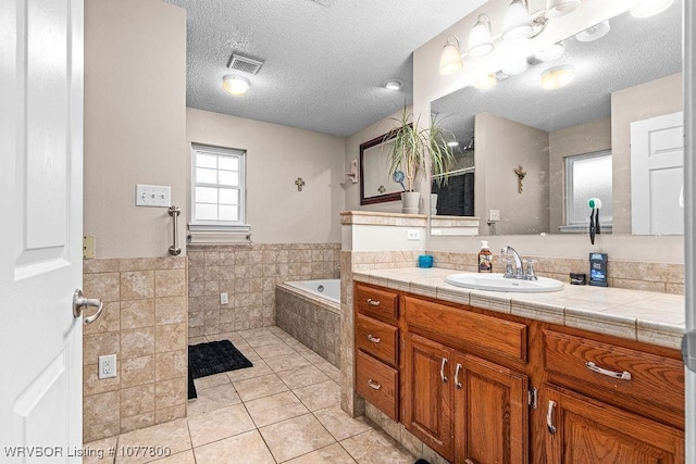 bathroom featuring vanity, tiled tub, tile patterned floors, and a textured ceiling