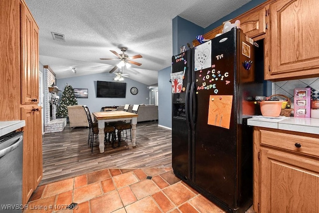 kitchen featuring tasteful backsplash, tile countertops, vaulted ceiling, black refrigerator with ice dispenser, and dishwasher