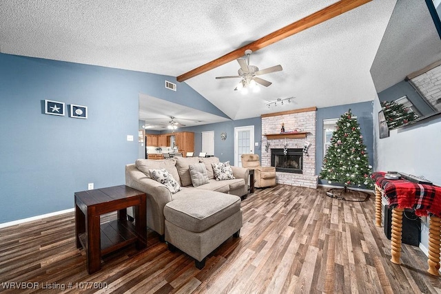 living room featuring vaulted ceiling with beams, wood-type flooring, a fireplace, and a textured ceiling