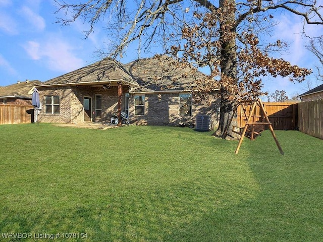 rear view of property featuring cooling unit, a fenced backyard, a yard, and brick siding