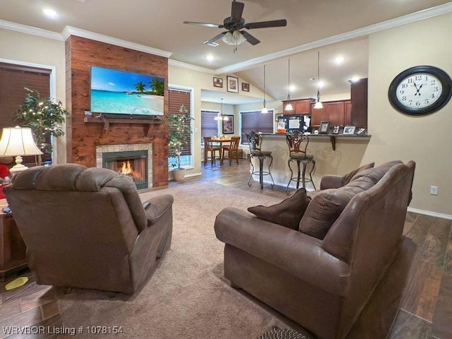 living room with ceiling fan, a fireplace, baseboards, vaulted ceiling, and crown molding