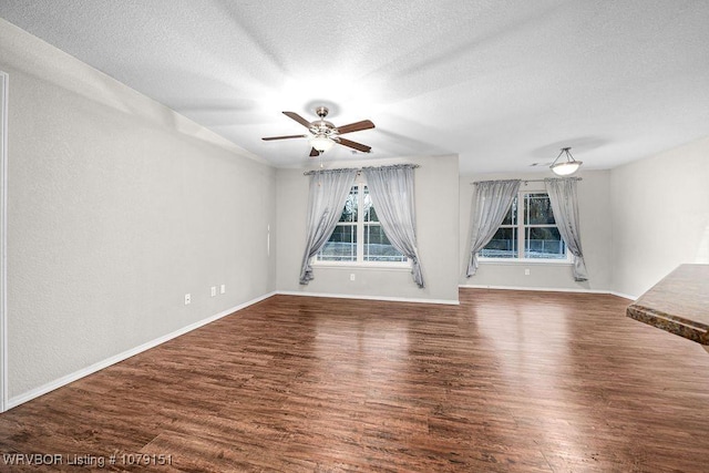 interior space featuring a textured ceiling, ceiling fan, dark wood-style flooring, and baseboards