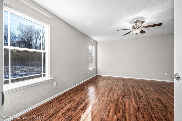 empty room featuring baseboards, a textured wall, ceiling fan, dark wood-type flooring, and a textured ceiling