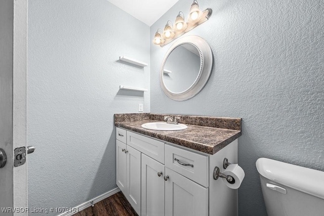 half bathroom featuring a textured wall, vanity, toilet, and wood finished floors