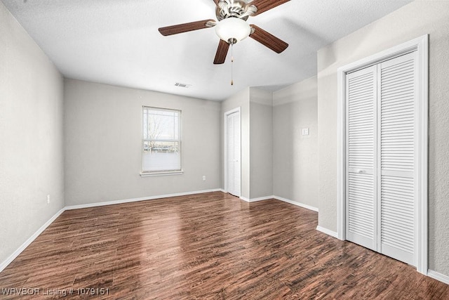 unfurnished bedroom featuring dark wood-style floors, baseboards, visible vents, and two closets