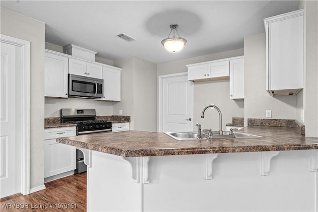 kitchen featuring a breakfast bar, dark countertops, appliances with stainless steel finishes, white cabinets, and a peninsula