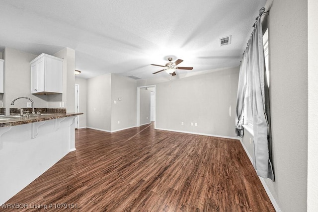 unfurnished living room with dark wood-style floors, a sink, visible vents, and baseboards