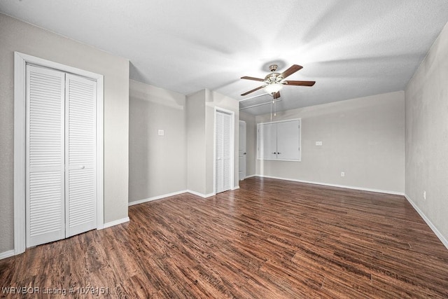 interior space with a ceiling fan, dark wood-style flooring, baseboards, and two closets